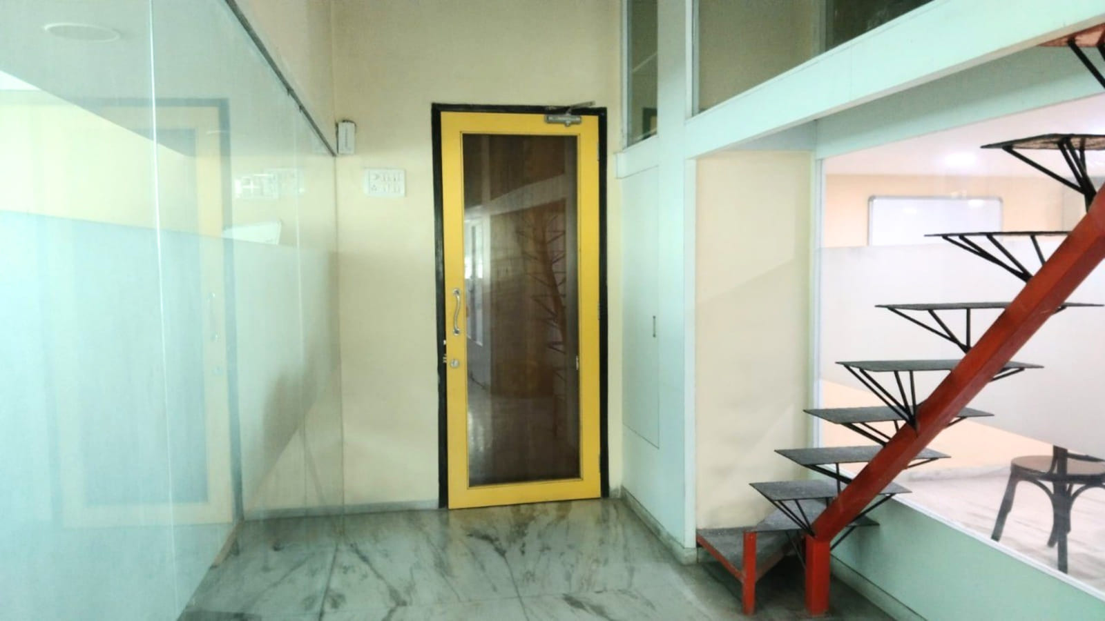 The Woosh Biz office entrance in Vashi — a yellow-framed glass door, frosted glass partitions and a red steel staircase up to the mezzanine