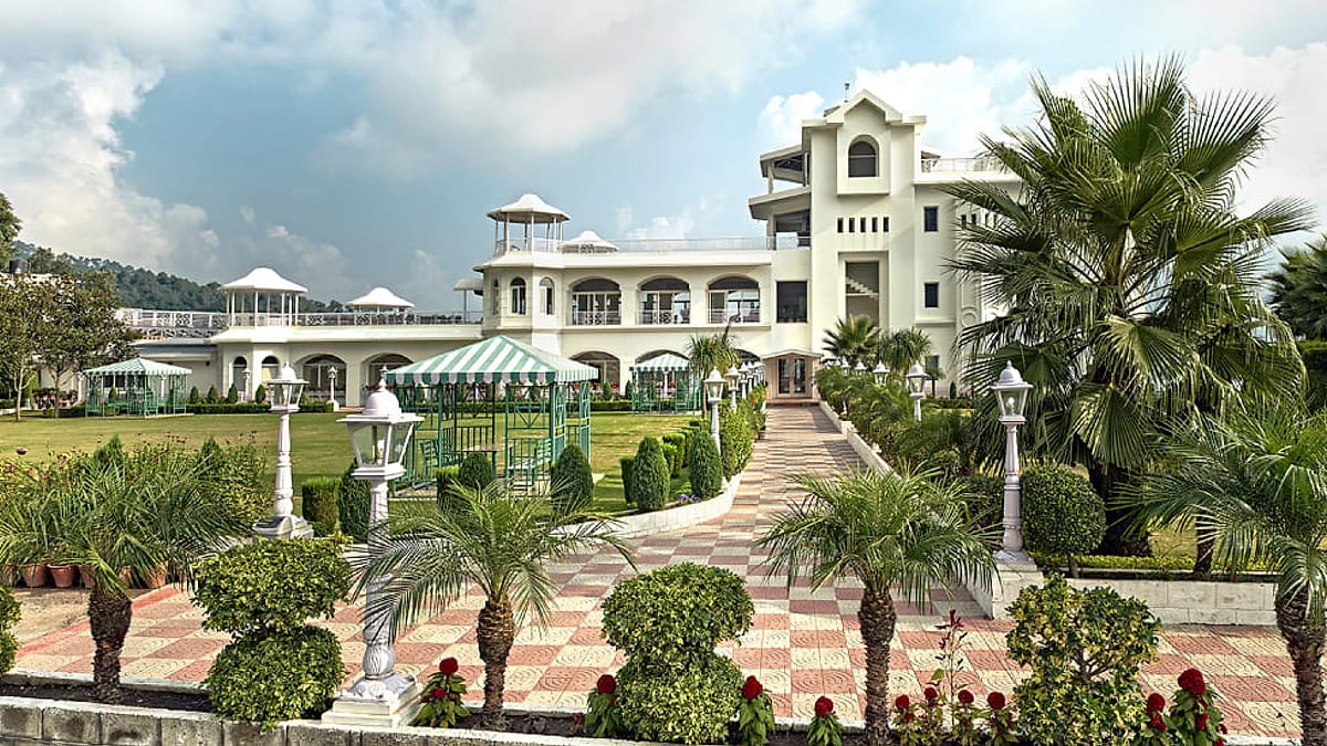 White colonial-style resort building behind clipped lawns, fountains and palm trees