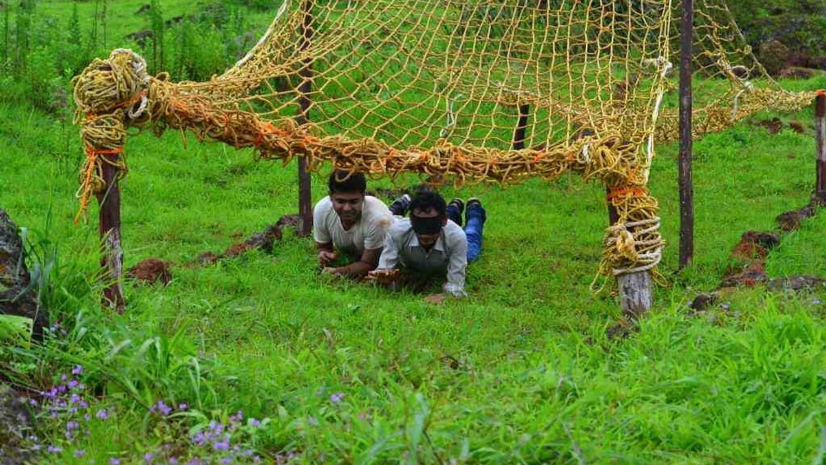 Rope commando net strung low across a grassy field with two people crawling under it