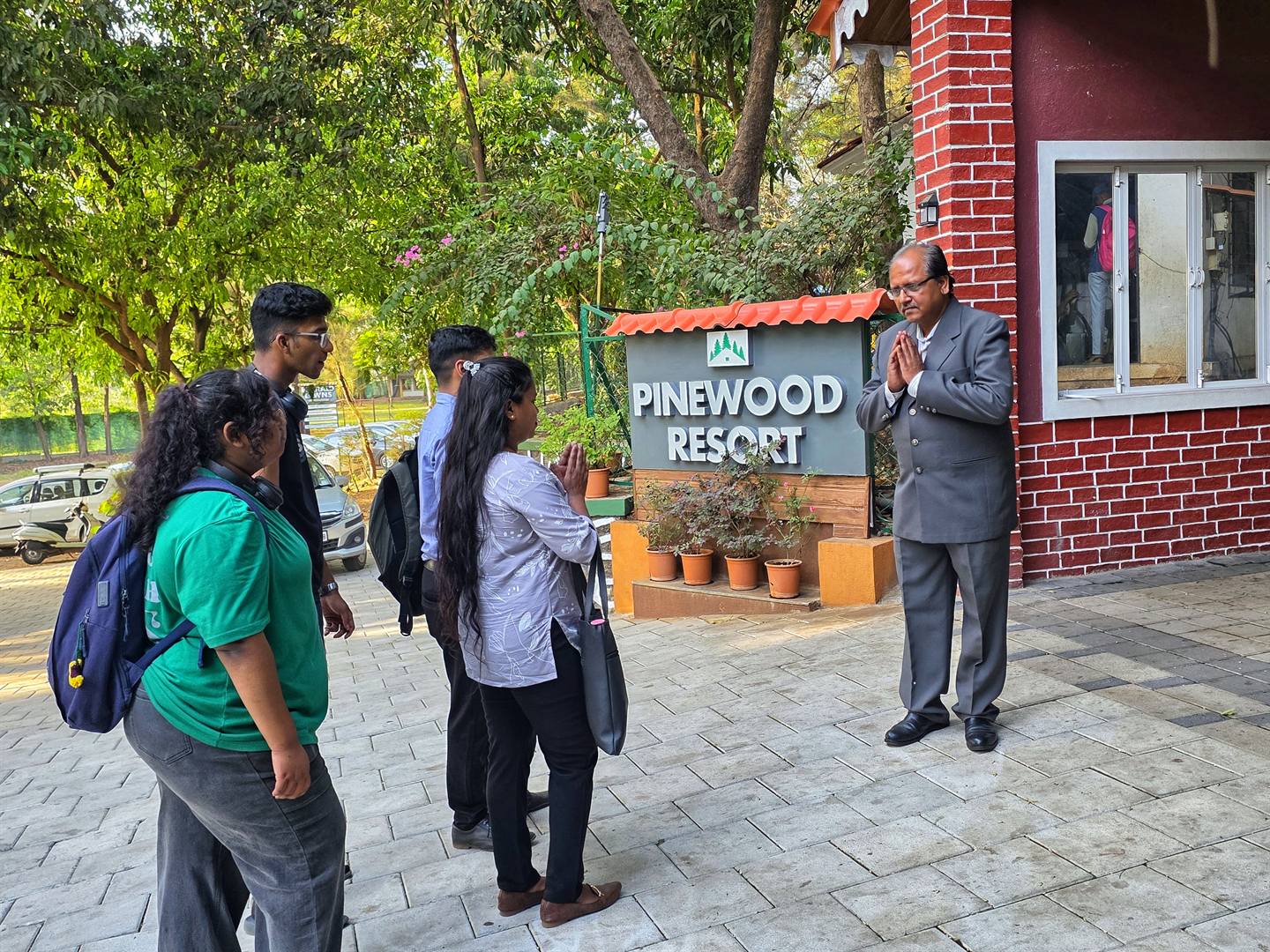 Pinewood Resort's host greeting a group of students with a namaste beside the resort's sign