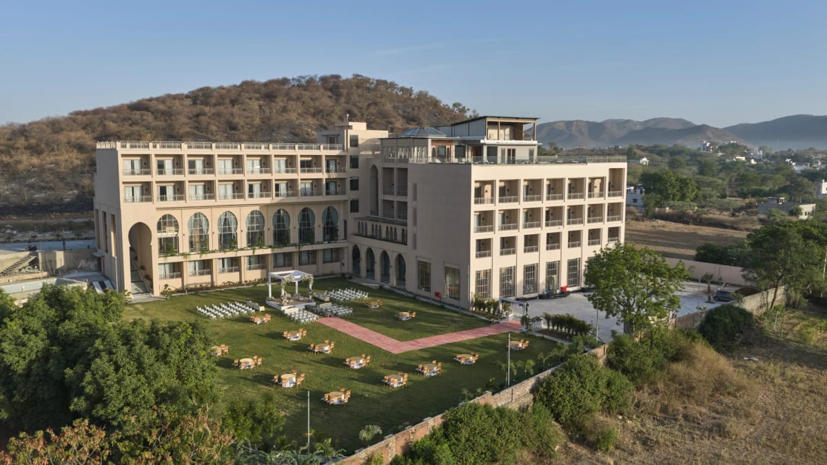 Aerial view of the resort's long white wing set in wide green grounds with hills behind